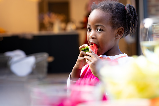Close-up of a young girl eating a large wedge of watermelon standing alone in the family garden. The house is located in Newcastle Upon Tyne, England.\n\nVideos are available similar to this scenario