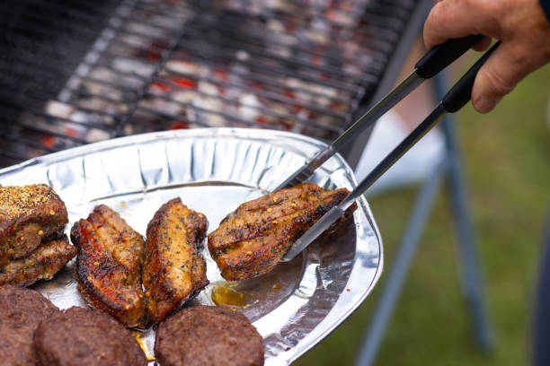 A close-up of a piece of seasoned pork is picked up by tongs that an unrecognisable person holds. The hot BBQ grill is in the background\n\nVideos are available similar to this scenario