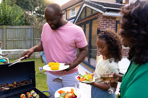 An over-the-shoulder shot of a multigenerational family having a BBQ in their family backyard. They are all wearing casual clothing and enjoying freshly prepared food. The house is located in Newcastle Upon Tyne, England.

Videos are available similar to this scenario
