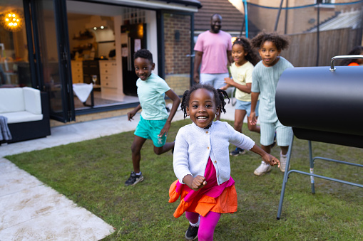 A wide shot of a group of children excitably playing in the garden chasing each other. They're looking into the camera all wearing casual clothing. They're located in Newcastle Upon Tyne, England.\n\nVideos are available similar to this scenario