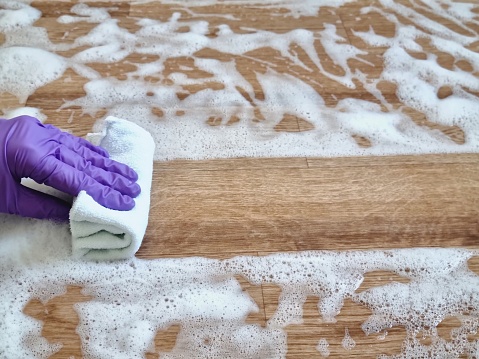 A hand in a purple rubber glove wipes solution from the floor with a cleaning rag