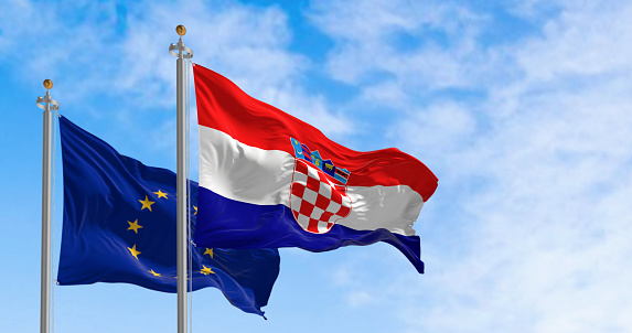 Flags of Croatia and the European Union waving in the wind on a clear day. Croatia has been a member of the eurozone since January 1, 2023. 3D illustration render. Fluttering fabric