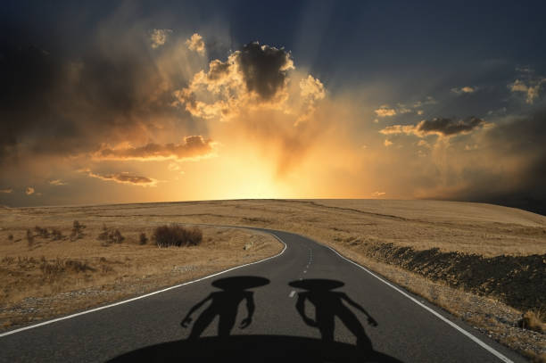 Shadows of two aliens on the road against the background of sunset