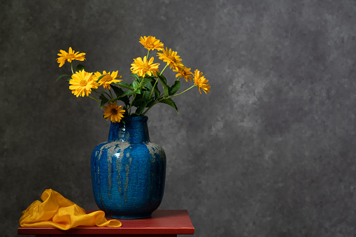 A bouquet of yellow autumn colors in a large blue vase on a dark gray background. Calm still life. Relax. Bright colors. Pleasure . Home interior.