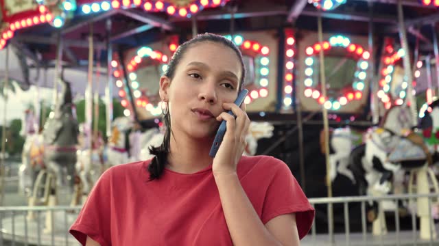 quality video of a young woman talking from an amusement park using her mobile phone for a work call