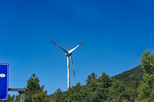 Scenic view of wind turbine at Griško polje with woodland on a sunny summer day. Photo taken August 11th, 2023, Griško Polje, Slovenia.