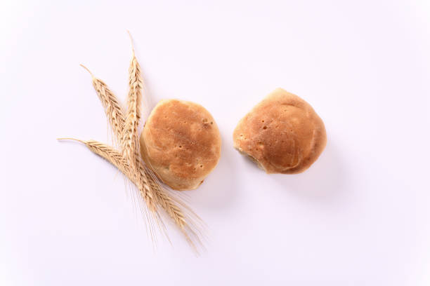 Freshly baked buns and ears of wheat on white background.