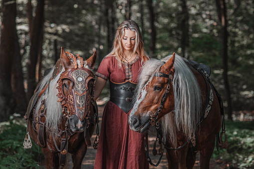 A beautiful female viking warrior queen in a woodland outdoor setting with horses