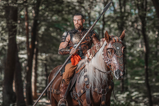 A handsome male viking warrior in a woodland outdoor setting with horses