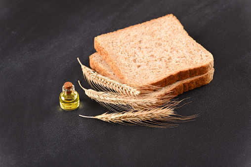 Raw toast bread with wheat ears and a bottle of oil on dark background.