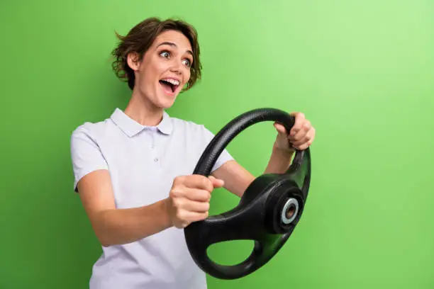 Photo of young woman brown hair crazy driver holding steering wheel fast porsche 911 automobile emotions isolated on green color background.