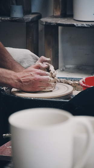 Pottery Wheel In Action: Craftsman Molding Clay With Skilled Hands. The Vertical Perspective Highlights The Artisan's Process And Tools In A Workshop Setting
