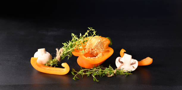 Mushrooms champignons and paprika with thyme sprig on a dark background.