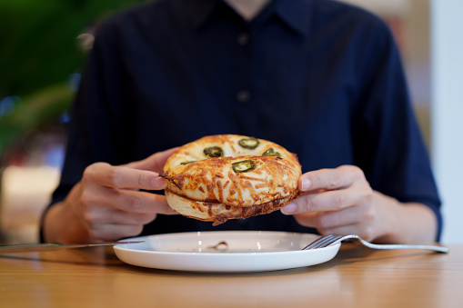 In the cropped image, a woman is seen enjoying a Jalapeno bagel for breakfast.