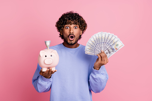 Photo of crazy cheerful guy open mouth wear trendy clothes showing piggy bank saving salary storage isolated on pink color background.