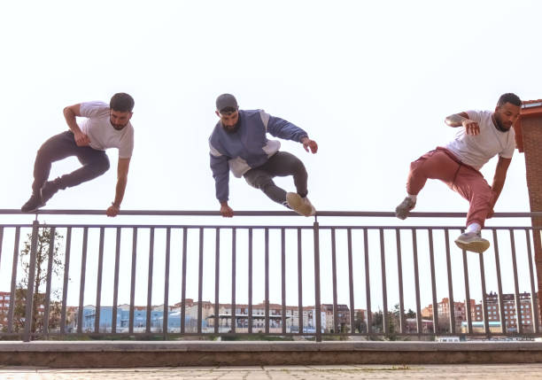 Groupof men men jumping a fence at once, with the city and the sky in the background, front view. Concept of parkour