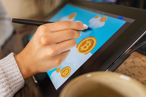 In her comfortable home office, a young artist brings bitcoin illustrations to life on her tablet.