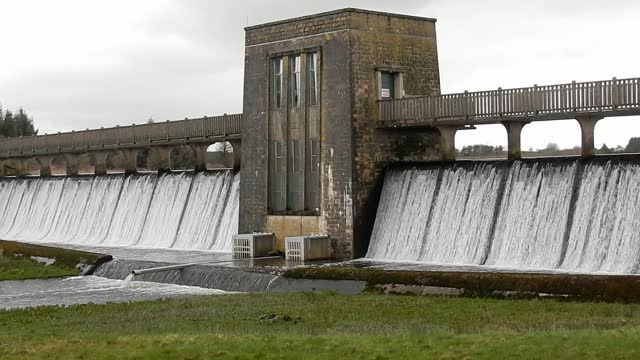 Llyn Cefni reservoir concrete dam gate overflowing from Llangefni lagoon, Anglesey rural scene