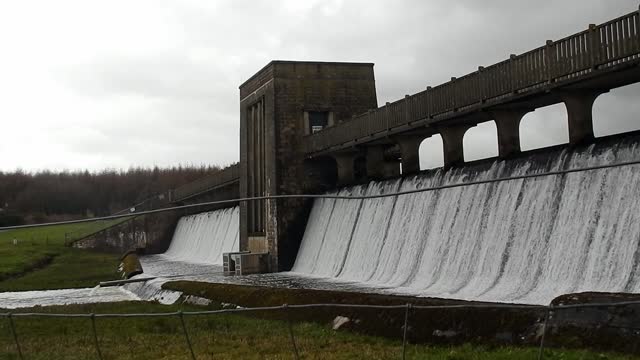 Llyn Cefni reservoir concrete dam gate bridge pouring from Llangefni lagoon, Anglesey rural scene