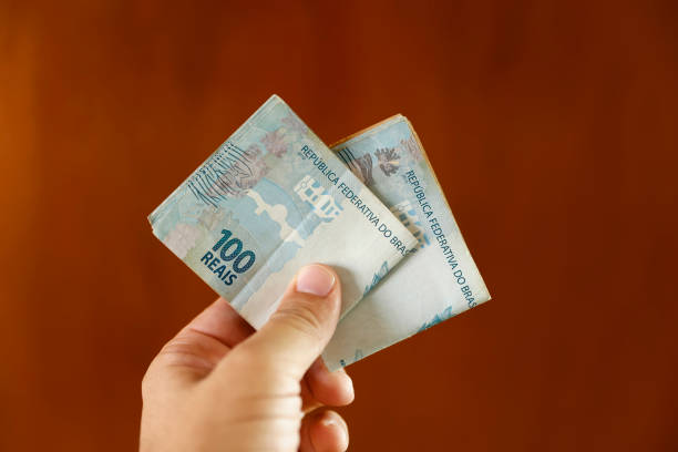 istock Brazilian money - hands with Brazilian real notes between fingers 2104048631