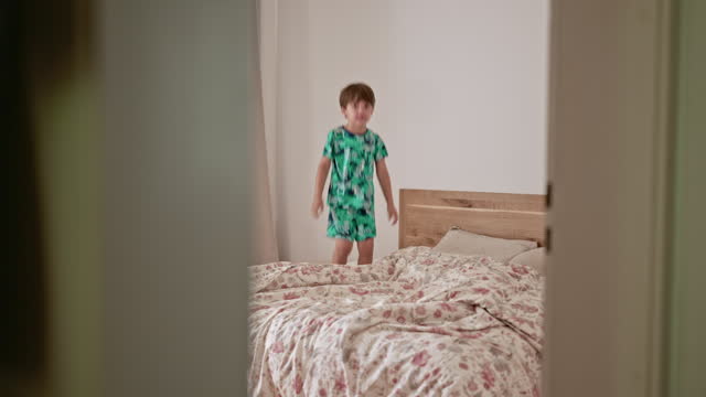 Happy Little Boy Jumping Up And Down On Parent's Bed. Candid Scene Of Energetic Child Enjoying Weekend Morning At Home