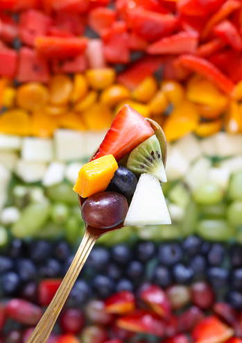 Stock photo showing a close-up, elevated view of a display of chopped multi-coloured fruits. Rainbow of chopped strawberries, watermelon, mango, physalis (Indian raspberries), honeydew melon, white grape, kiwi, blueberries, plums and red grapes. Healthy eating concept.