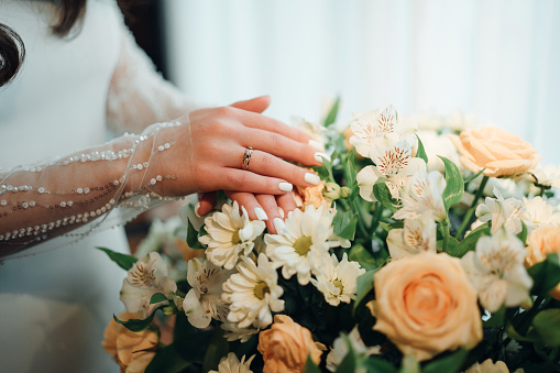Bride's hands with wedding ring on bouquet. A symbol of love and loyalty.