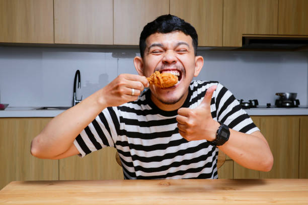 istock Funny asian man eating fried chicken and eggs at the kitchen 2104072666