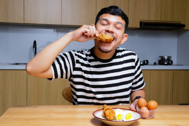 istock Funny asian man eating fried chicken and eggs at the kitchen 2104073713