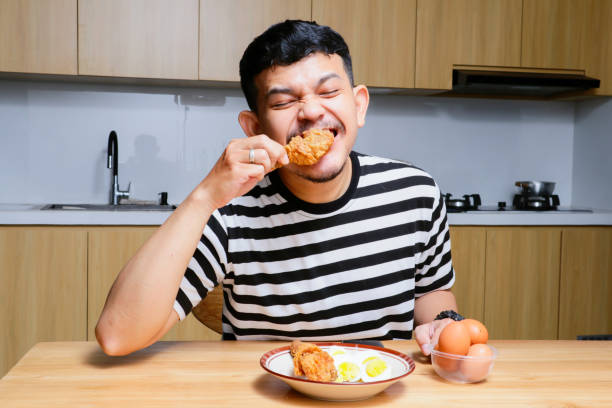 istock Funny asian man eating fried chicken and eggs at the kitchen 2104074253