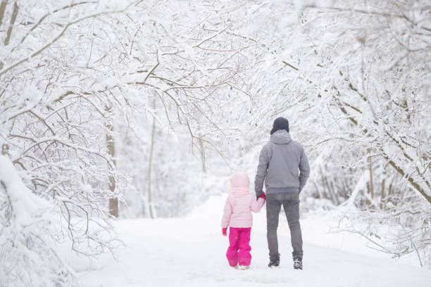 istock Father and daughter walking on white fresh snow covered road through tree branches at park after blizzard. Spending time together in beautiful cold winter day. Enjoying nature stroll. Back view. 2104095191