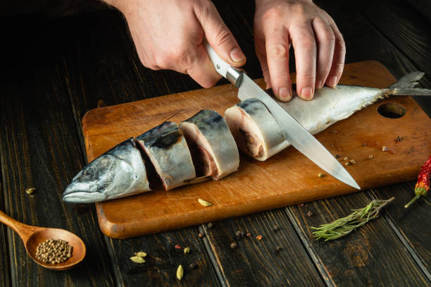 istock The cook cuts raw fish with a knife before baking it on the grill. Spices on the kitchen table for preparing a delicious breakfast with mackerel 2104104533