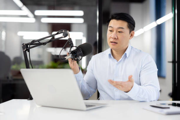 istock Concentrated korean male recording podcast with professional microphone while looking at laptop screen. Focused financial blogger making new informative content for web site with investment options 2104106606