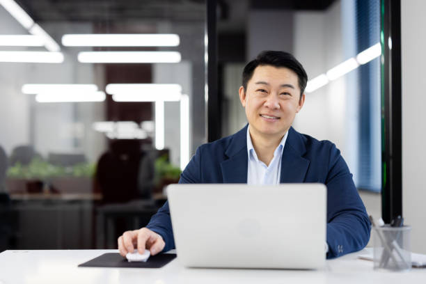 istock Confident asian businessman smiling while working on laptop in modern office space 2104108717