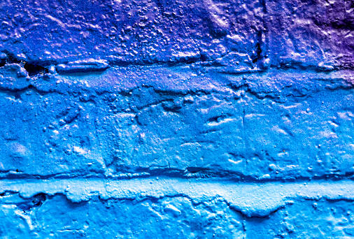 Macro image of some rough bricks and cement in a brick wall surface, spray painted blue and purple.