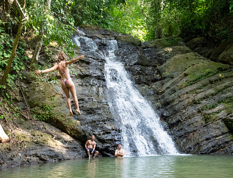 Poza Azul waterfall is set in the jungle of Dominicalito. It has a natural swimming pool. The site is a popular for swimming and jumping into the small pond from a swinging rope. Image shows a diver in mid air.\nDominical, Costa Rica.\n01/23/2023