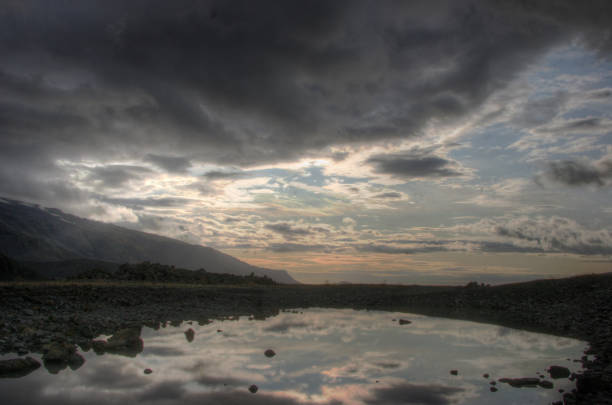 le nuvole pesanti al tramonto si posano su un piccolo lago in islanda - mountain alpenglow glowing lake foto e immagini stock