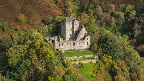 Oban, United Kingdom – July 12, 2024: A historic stone castle surrounded by green gardens and scenic mountains under a cloudy sky in Scotland