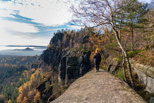 A middle-aged woman travels the world. Stands against the backdrop of majestic mountains in the national park of Saxony, Bastei, Switzerland, Germany.
