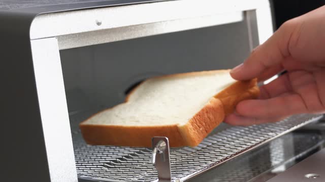 A man's hand baking bread in a toaster oven.