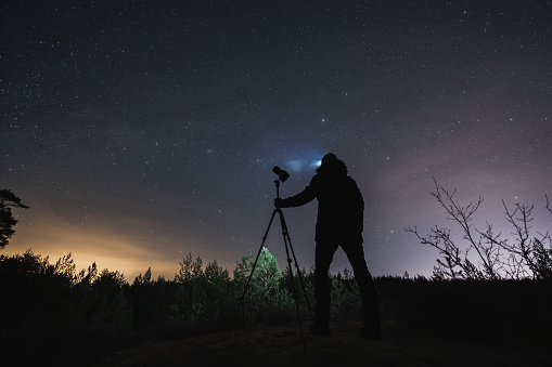 Landscape astrophotographer with a camera on a tripod outdoors in early spring at night under the starry sky.High quality photo