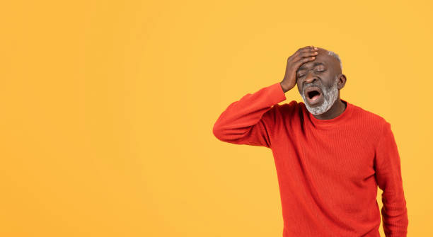istock Elderly man in red sweater and hat holding his head with an agonized expression 2104160749