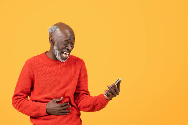 istock Joyful elderly man in a red sweater laughs while looking at a smartphone 2104160761