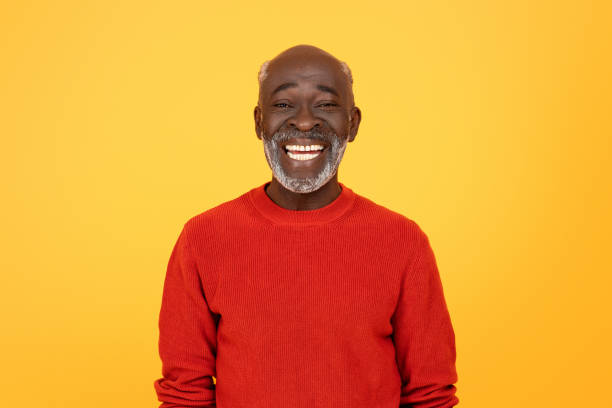 Radiant senior Black man with a white beard, sporting a red sweater and a beaming smile Radiant glad senior african american man with a white beard, sporting a red sweater and a beaming smile, standing confidently against a monochrome yellow studio background black man stock pictures, royalty-free photos & images