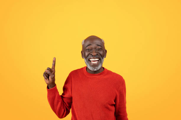 istock Joyful elderly Black man with white beard laughing and pointing upwards, wearing red sweater 2104161354