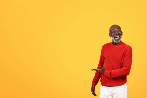 istock Joyful senior Black man in a red sweater laughing and presenting something to his side 2104161361