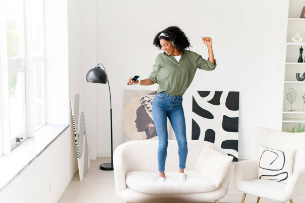 istock In a dynamic pose, the woman dances on a couch with her smartphone in hand 2104185277
