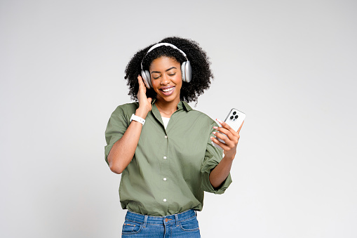 African-American woman with headphones, smiles at her phone, likely enjoying a lighthearted conversation or listening to a favorite tune, highlighting the joy of leisure amidst business.