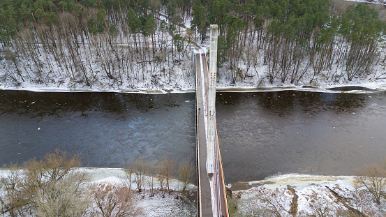 Drone photography of a footbridge going over river from city to public park during winter cloudy day