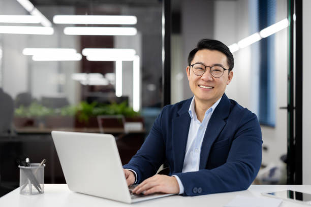 Portrait of successful mature asian businessman, experienced boss in business suit smiling and looking at camera, financier investor inside office at workplace working with laptop, satisfied man. retrato de exitoso hombre de negocios asiático maduro, jefe experimentado en traje de negocios sonriendo y mirando a la cámara, inversor financiero dentro de la oficina en el lugar de trabajo que trabaja con computadora portátil, hombre satisfecho